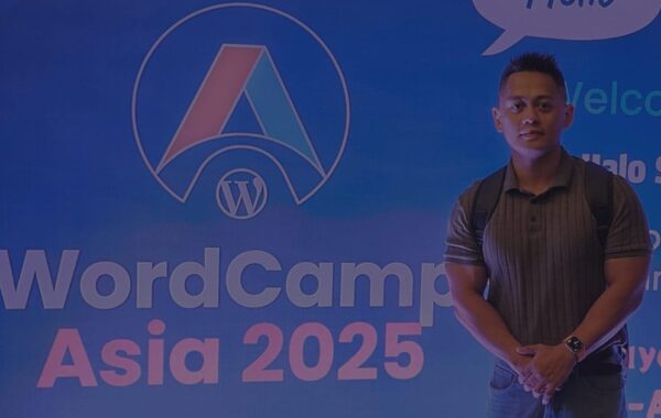 Attendee at WordCamp Asia 2025 standing in front of the official event backdrop in the registration desk featuring the WordPress logo.