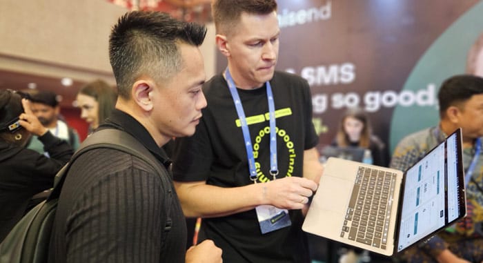 WordCamp Asia 2025 attendee engaging with a tech exhibitor at a booth, discussing a WordPress-related tool on a laptop. A key networking opportunity for developers, designers, and digital professionals.
