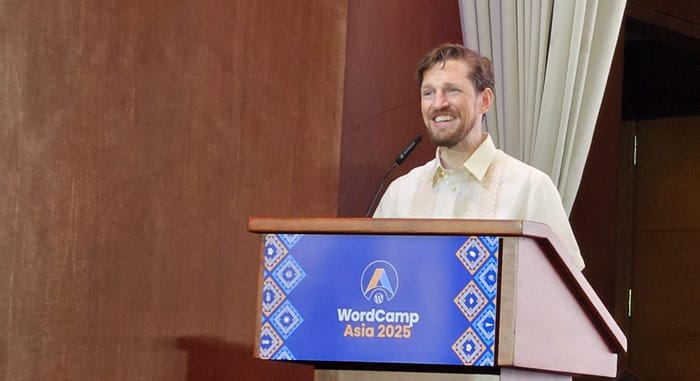 Matt Mullenweg delivering a speech at WordCamp Asia 2025, standing at a podium with the event’s branding.