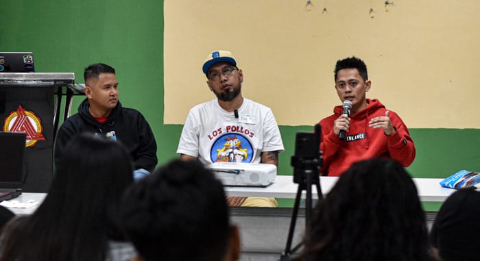 Three panelists speaking at a WordPress Meetup, one holding a microphone while addressing the audience. A camera records the session from the front row.