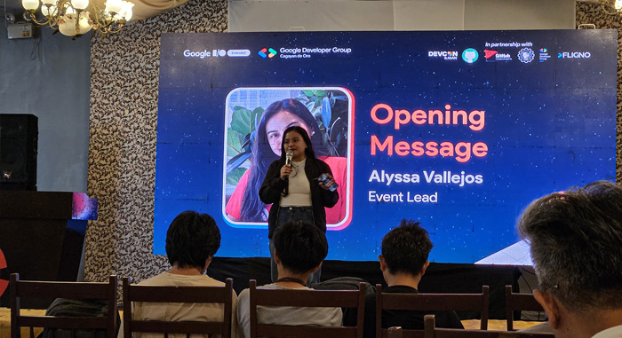 lyssa Vallejos, the GDG Cagayan de Oro Event Lead, stands on a stage with a microphone, giving the opening message for the Google I/O Extended event.